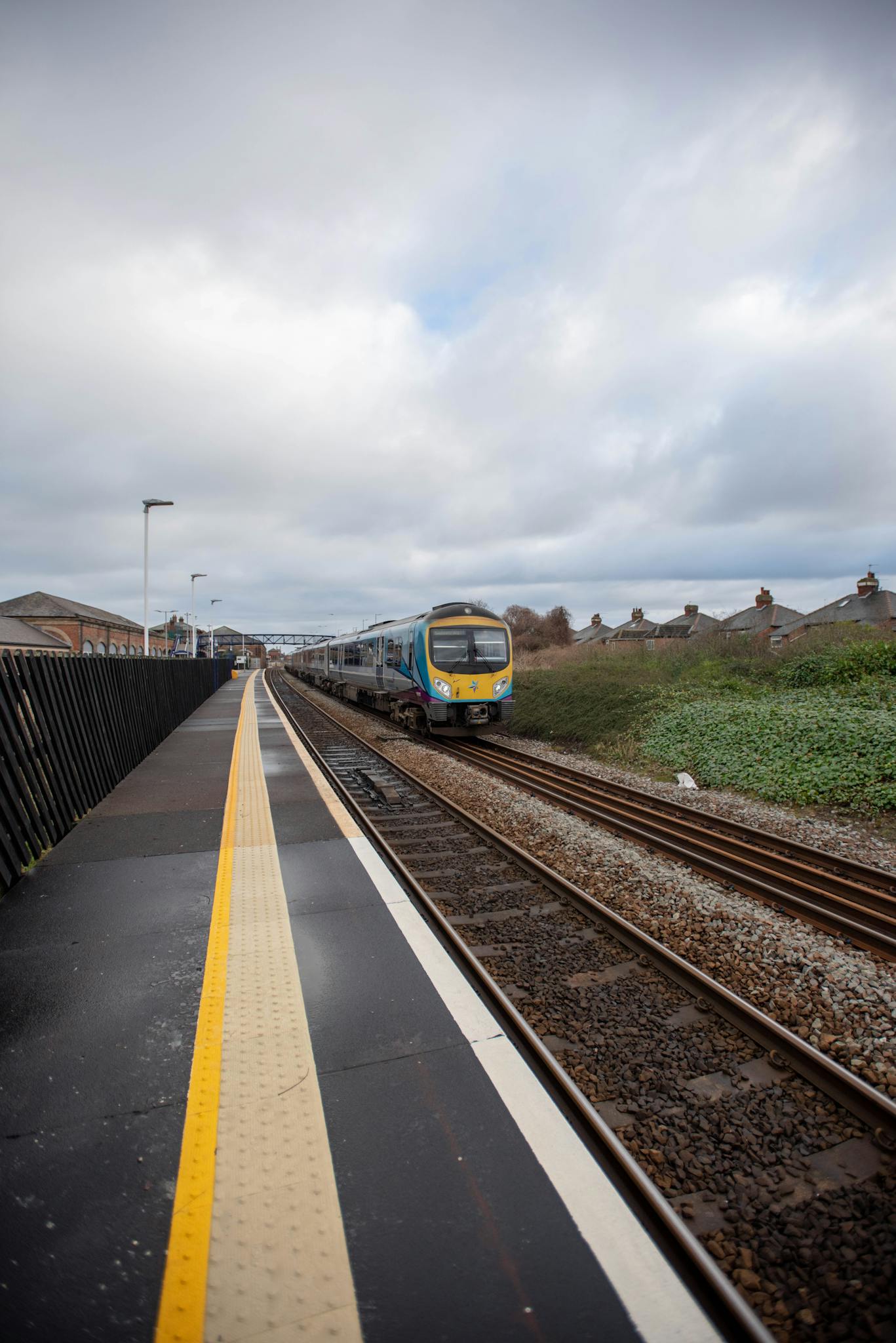 A commuter train approaches an empty platform under a cloudy sky, symbolizing travel and movement.