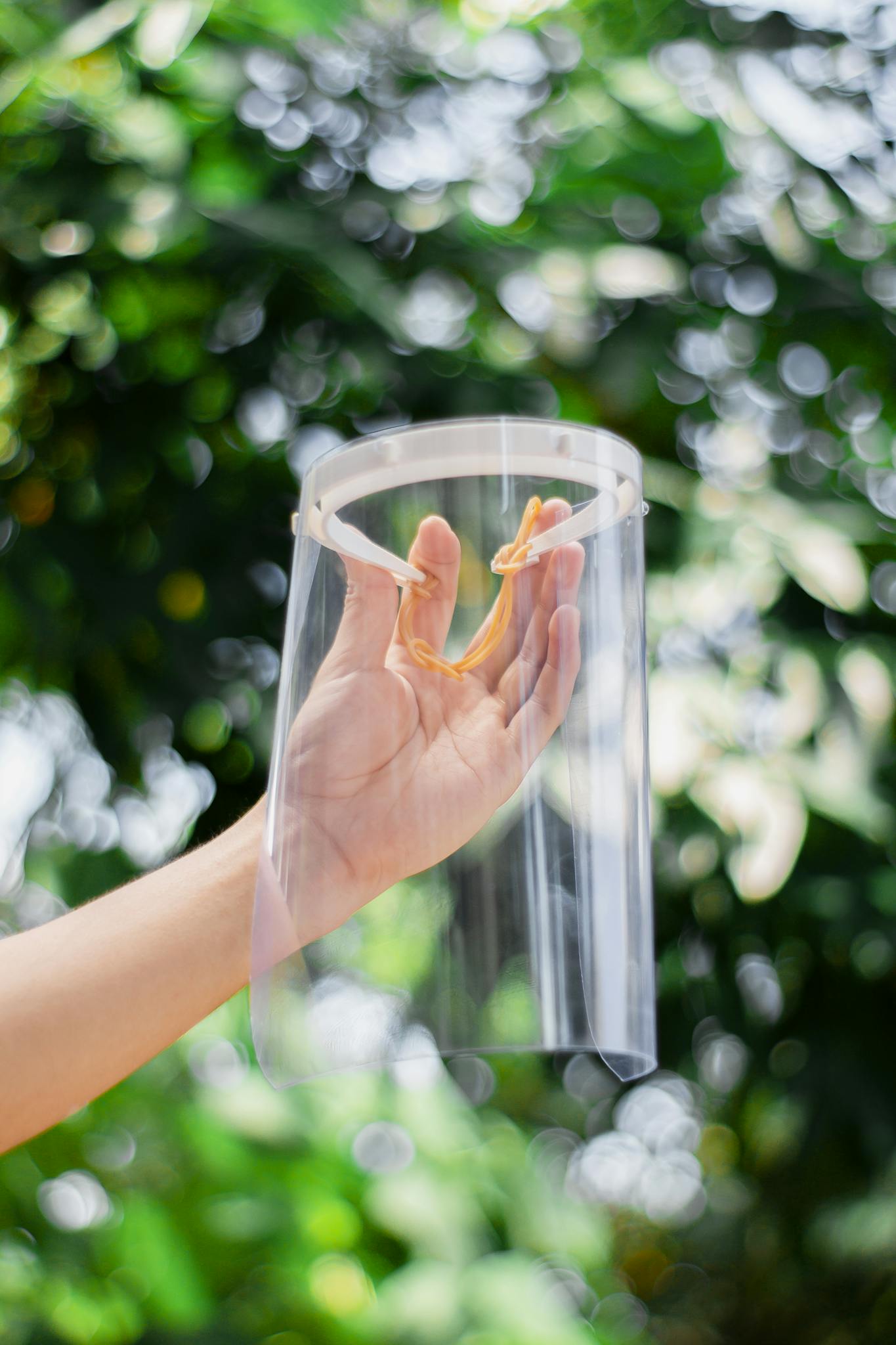A hand holding a clear face shield against a vibrant, blurred green background.